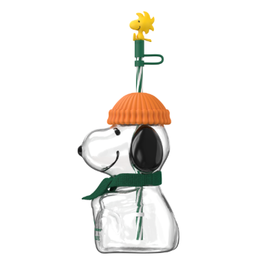 A Snoopy-shaped clear glass vase with an orange knit hat, green scarf, and a yellow Woodstock topper on a white background.